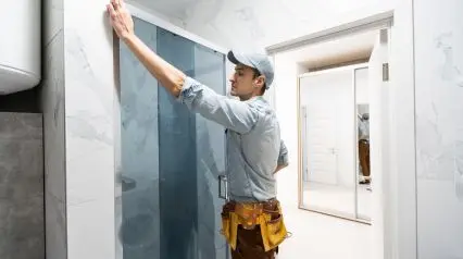 a repairman fixing shower doors in a hotel as part of the tasks in a hotel maintenance checklist|Hotel Maintenance Checklist Sample Report|Hotel Maintenance Checklist