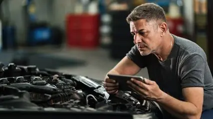 a car technician repairing a car while referring to a repair order form using a tablet|Repair Order Form Sample Report|Repair Order Form