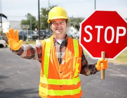 Friendly construction worker in the road holding up a stop sign