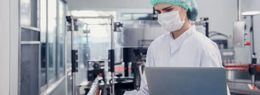 a manufacturing supervisor inspecting production using product compliance software on a laptop