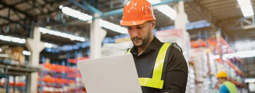 worker using a supply chain risk management software on their laptop in a warehouse