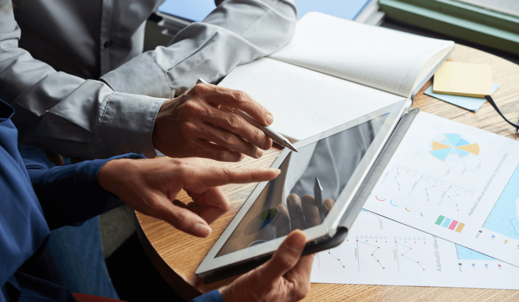 Two professionals reviewing compliance reports and risk analysis charts on a tablet and printed documents.