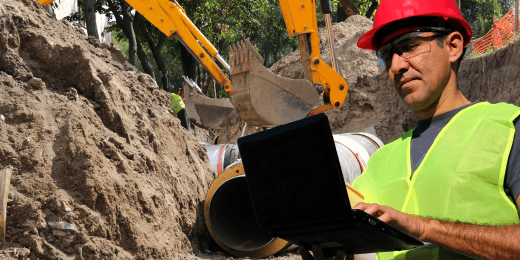 Man in construction site creating a trench and holding a laptop