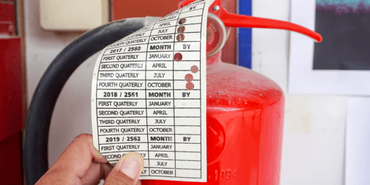 A fire extinguisher inspection tag attached to the nozzle of the extinguisher, showing the months of maintenance and inspections completed