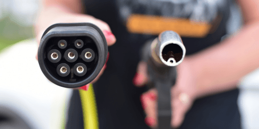 Person holding an electric vehicle charging plug and a fuel pump nozzle side by side.
