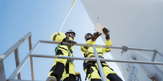 Two wind turbine engineers in safety gear inspecting a wind turbine using a tablet.