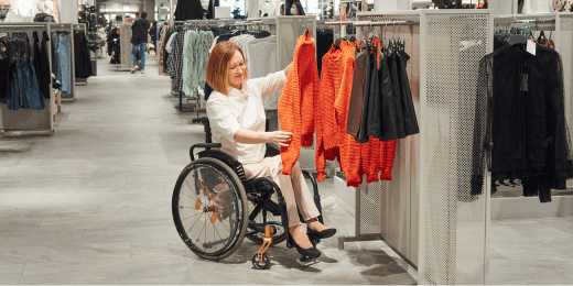 A woman in a wheelchair shopping for clothes in a retail store.