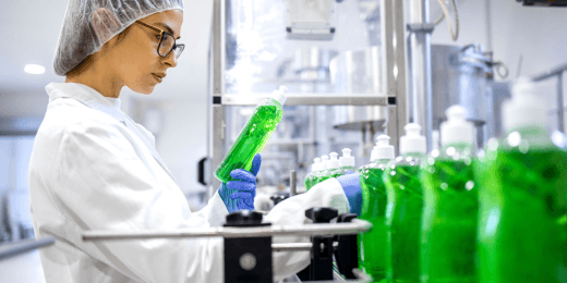 A quality control technician inspects a bottle of green liquid soap on a production line during the soap manufacturing process.