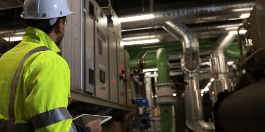 Engineer inspecting industrial HVAC equipment with a tablet in a mechanical room.
