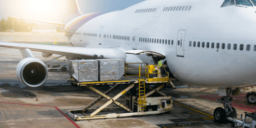 Ground crew loading cargo into the belly of a large commercial airplane on the tarmac using a hydraulic lift.