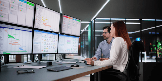 Man and woman in front of multiple computer screens showing digital analytics and business data