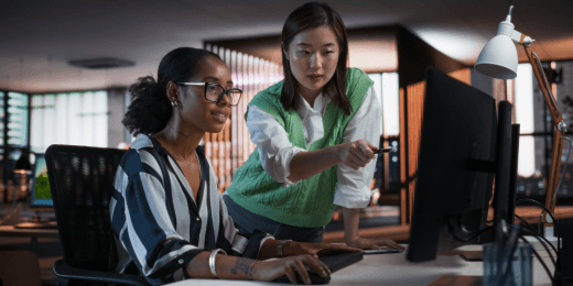 Two female coworkers at a work desk discussing work instructions