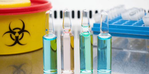 Glass ampoules with colored liquids next to a yellow biohazard container and a blue test tube rack in a laboratory setting.
