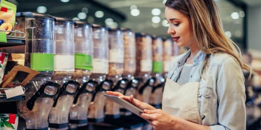 Female store employee with tablet checking bulk food dispensers in a supermarket.