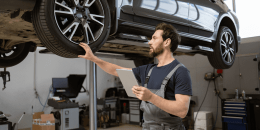 Mechanic inspecting a car tire while holding a tablet in an auto repair shop.