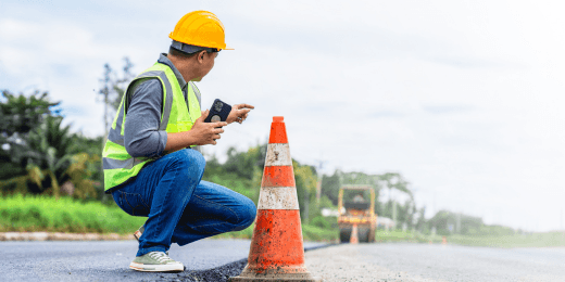 A construction worker holding a phone while placing a traffic cone in a road work zone for safety.