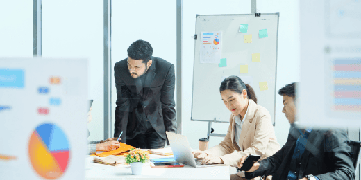 Group of business professionals collaborating in a modern office meeting room with charts and notes on a whiteboard.