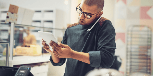Man in a shop using a tablet while talking on the phone.