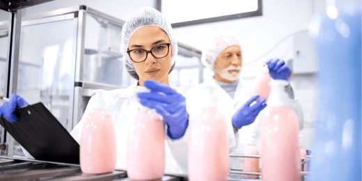 Workers in protective clothing inspecting pink cosmetic bottles on a production line in a manufacturing facility.