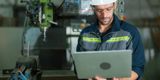 Industrial worker in front of equipment, reading work instructions off a laptop