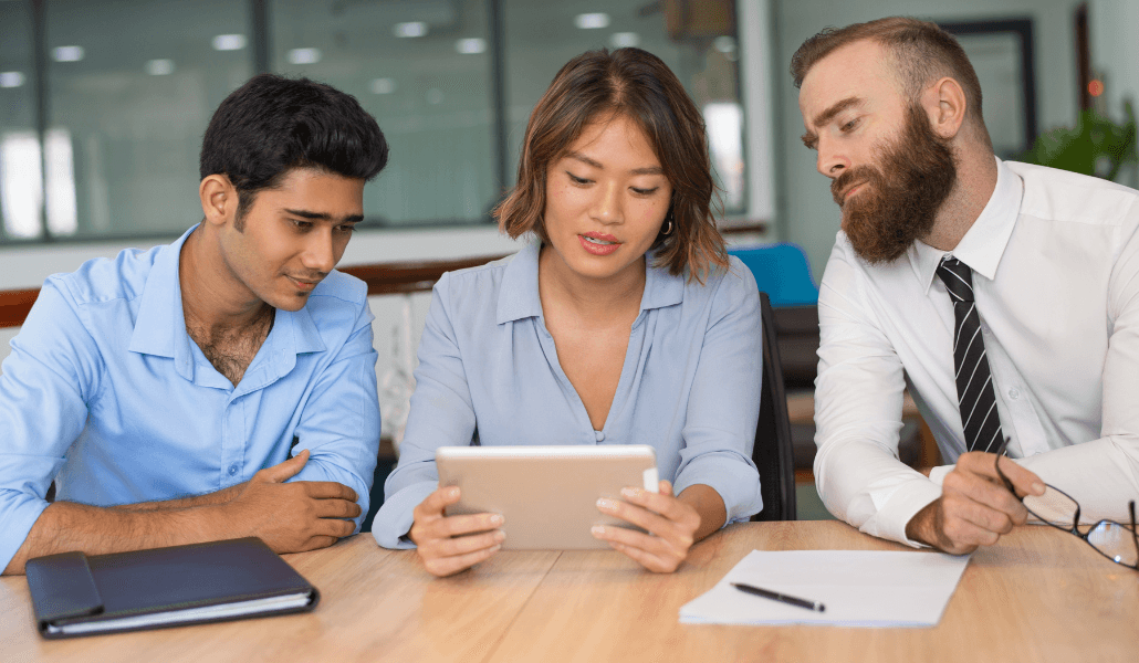 Three colleagues reviewing information on a tablet during a workplace meeting.