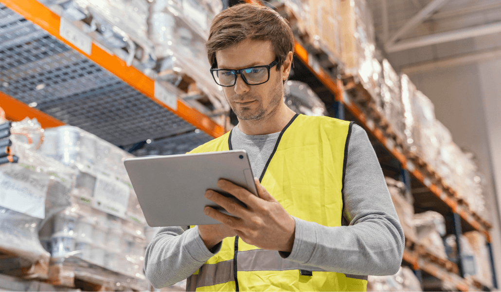A warehouse worker reviewing supply information on a tablet.