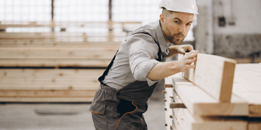 A construction worker in a hard hat inspecting wooden planks inside a workshop.