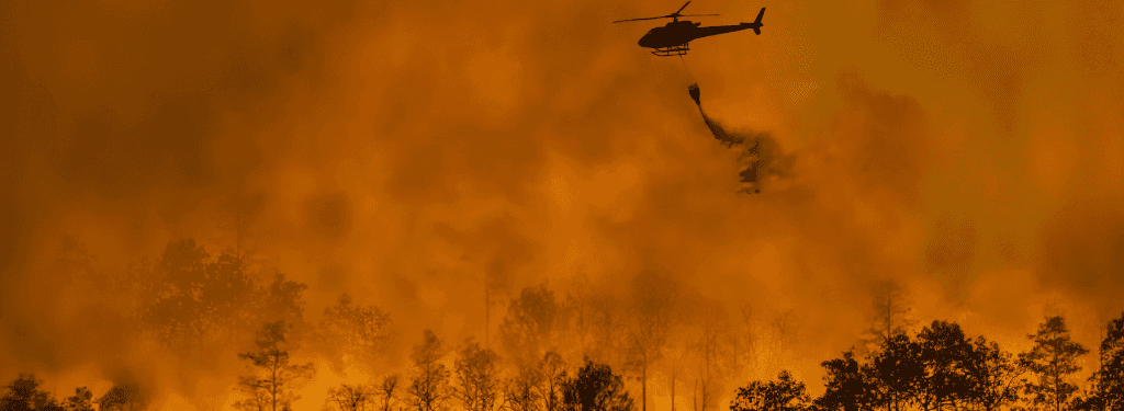 A helicopter dropping fire retardant on a wildfire.