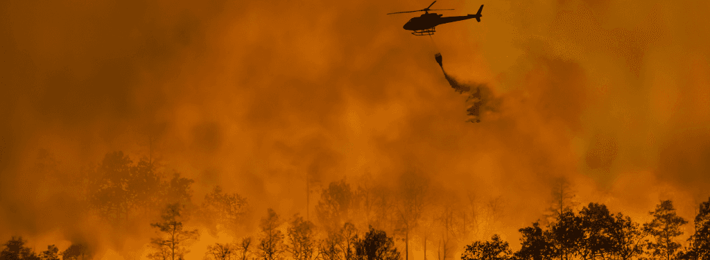 A helicopter dropping fire retardant on a wildfire.