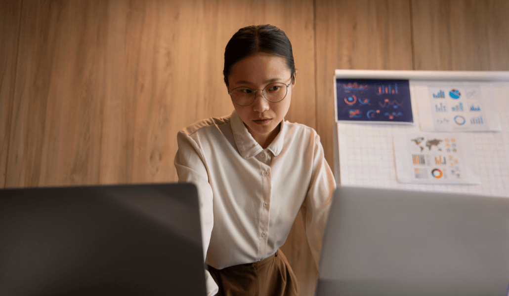 Person analyzing risk data charts on dual monitors with a data visualization board in the background