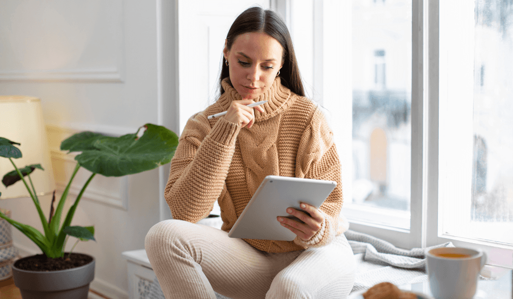A stress-free woman sitting by the window with a cup of coffee and her tablet.
