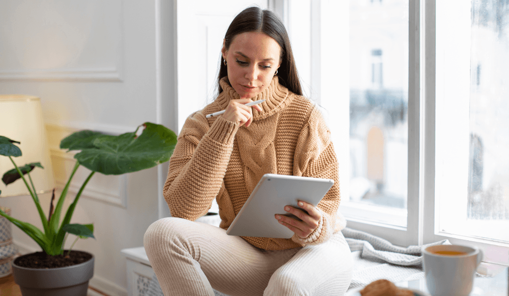A stress-free woman sitting by the window with a cup of coffee and her tablet.