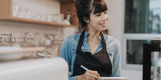 Smiling barista wearing an apron while taking notes in a cafe.