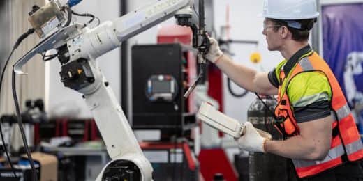 Worker performing maintenance on a robot. Some tasks are automated by the machine or tablet in their hand while they inspect the robot's arm.