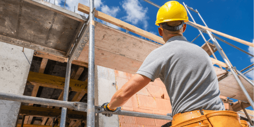 A construction worker stands on scaffolding to perform necessary repairs resulting from deferred maintenance.