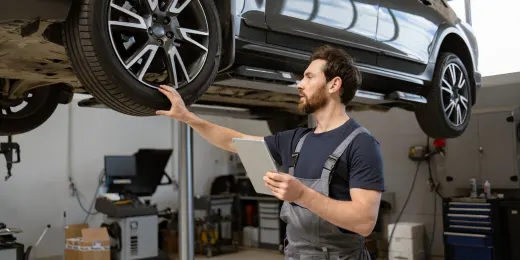 Mechanic inspecting a car tire while holding a tablet in an auto repair shop.