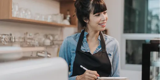 Smiling barista wearing an apron while taking notes in a cafe.