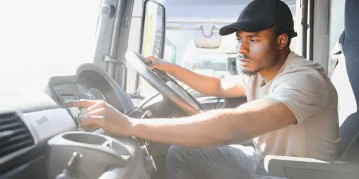 Man conducting a CDL pre-trip inspection inside a truck cab.