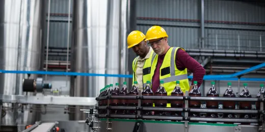 Two factory line workers inspecting bottled drinks on a production line.