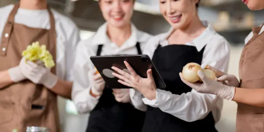 Kitchen staff using a food prep checklist on their tablet while preparing ingredients.